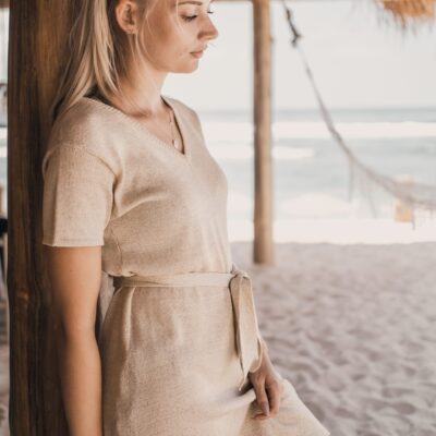Vertical shot of a woman standing next to a wooden column on sand
