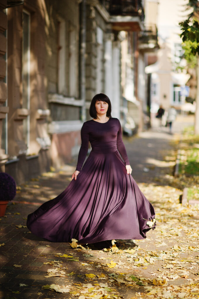 Adult brunette woman at violet gown on autumn fall background.