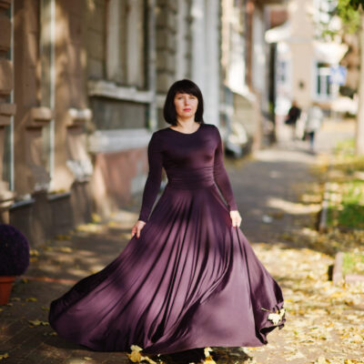 Adult brunette woman at violet gown on autumn fall background.