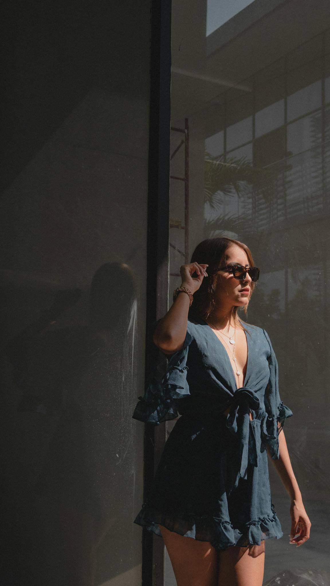 Fashionable woman in sunglasses posing outside in natural light, showcasing modern outfit.
