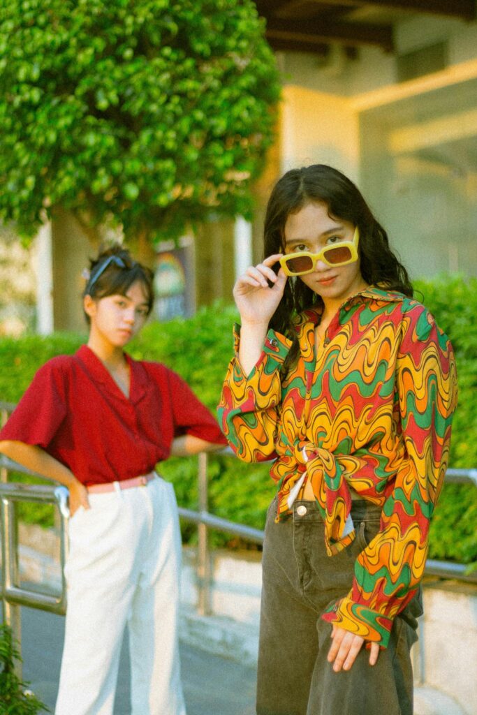 Two fashion-forward women pose outdoors in colorful outfits with stylish sunglasses, exuding confidence.