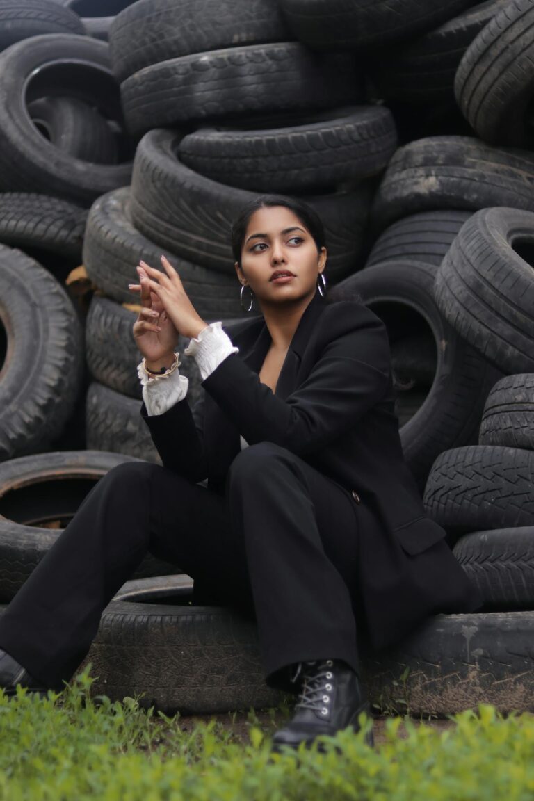 Woman in black blazer sitting against a backdrop of stacked tires, looking contemplative.